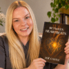 Zoë Castle, author of Between Heartbeats, holding her book inspired by her experiences living with 22q11.2 deletion syndrome.
