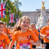 Children and families wearing orange Children with Cancer UK shirts take part in the Westminster Mile in London, with Buckingham Palace behind them.