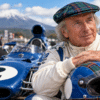 Sir Jackie Stewart-inspired racing portrait beside a classic blue Formula 1 car, wearing a tartan cap and resting his hands on a racing helmet, with Mount Fuji in the background.